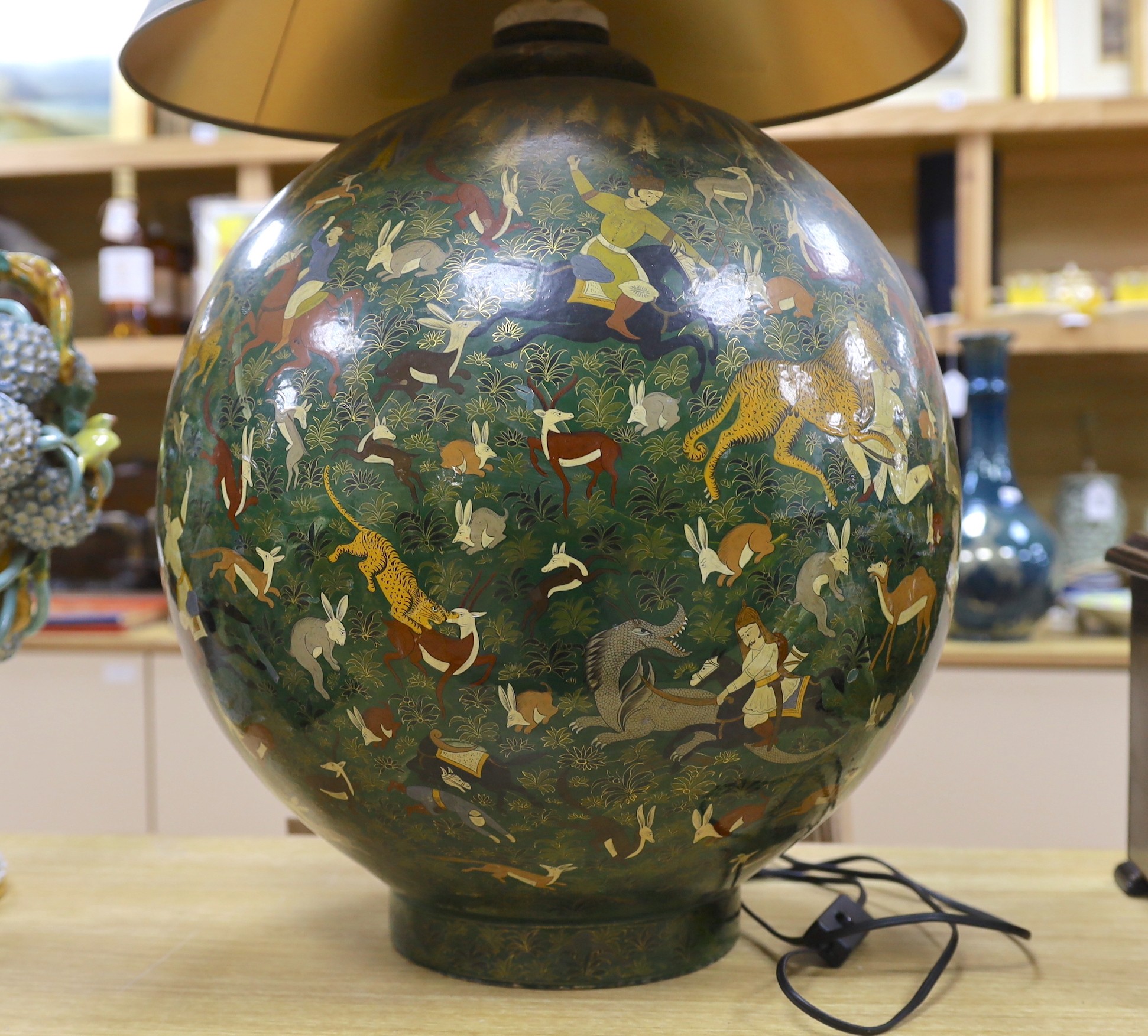 An Indian spherical green ground papier mache table lamp, decorated with hunting scenes and green shade, 75cms high including shade